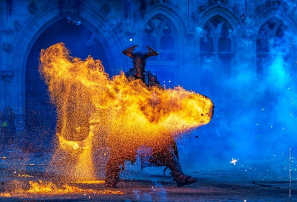 Performer en tenue de Diablo, braises en staff — contraste entre le fond bleu et le premier plan doré